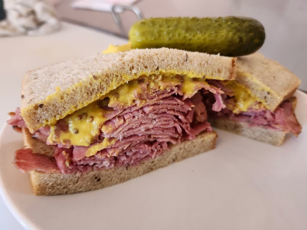Smoked meat sandwich with mustard on rye, served with a pickle